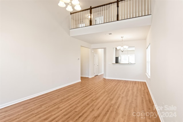 unfurnished living room featuring light hardwood / wood-style floors, a high ceiling, and an inviting chandelier