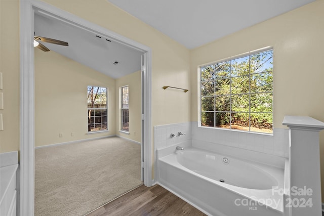 bathroom with wood-type flooring, a tub to relax in, vaulted ceiling, and a wealth of natural light