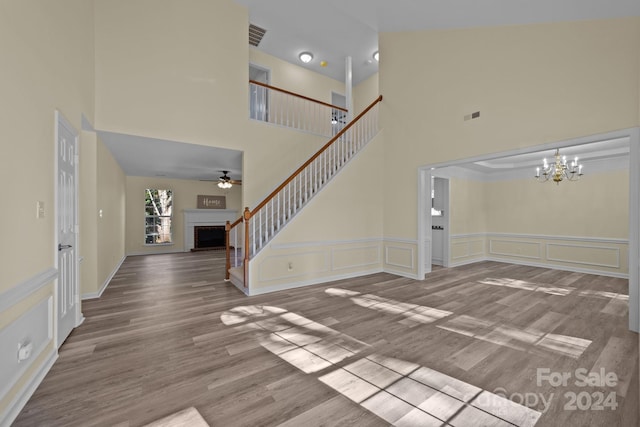 unfurnished living room with a high ceiling, ceiling fan with notable chandelier, and hardwood / wood-style floors