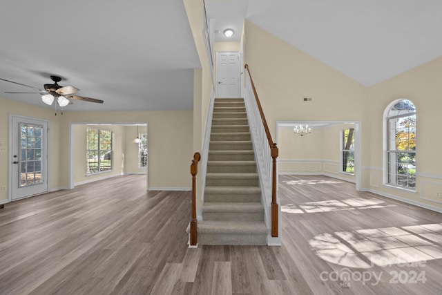 stairway featuring hardwood / wood-style flooring, ceiling fan with notable chandelier, and high vaulted ceiling