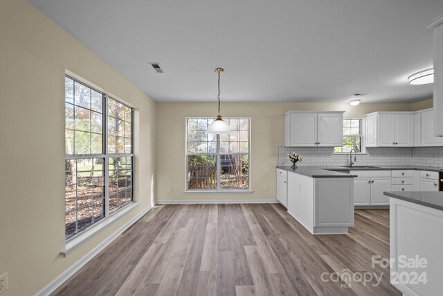 kitchen with sink, light hardwood / wood-style flooring, decorative backsplash, decorative light fixtures, and white cabinetry