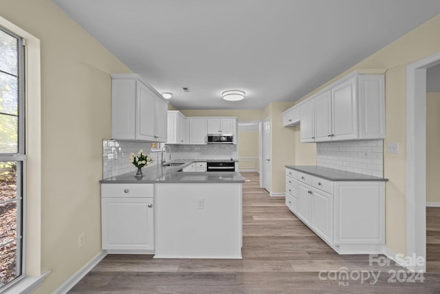 kitchen featuring kitchen peninsula, light wood-type flooring, backsplash, sink, and white cabinetry