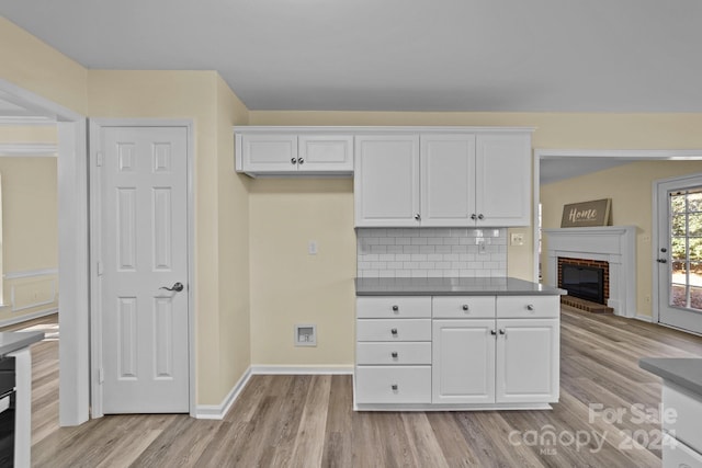 kitchen with decorative backsplash, a fireplace, white cabinets, and light wood-type flooring