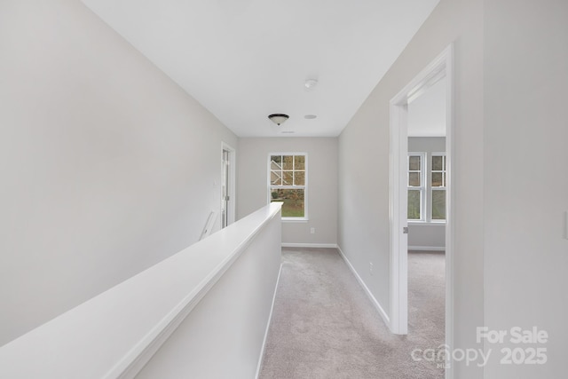 hallway featuring light carpet, baseboards, and an upstairs landing