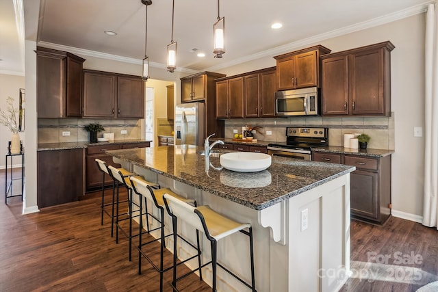 kitchen featuring ornamental molding, a center island with sink, a kitchen bar, dark wood finished floors, and appliances with stainless steel finishes