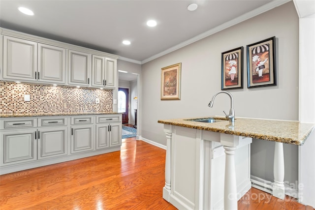 kitchen with light stone countertops, decorative backsplash, sink, light hardwood / wood-style flooring, and crown molding