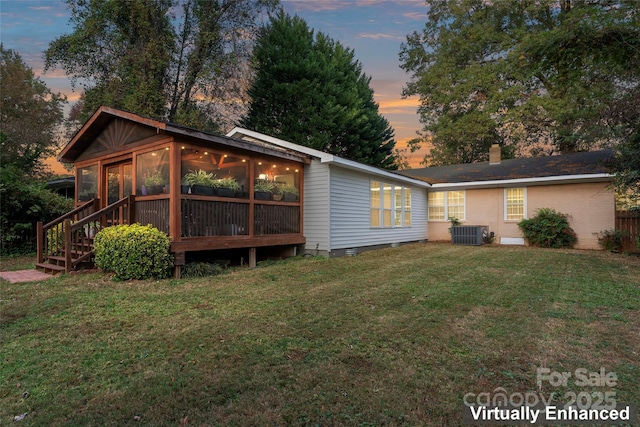 back house at dusk with central AC unit, a yard, and a sunroom