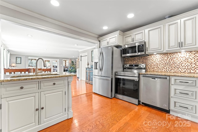 kitchen with tasteful backsplash, appliances with stainless steel finishes, ornamental molding, light wood-type flooring, and a sink