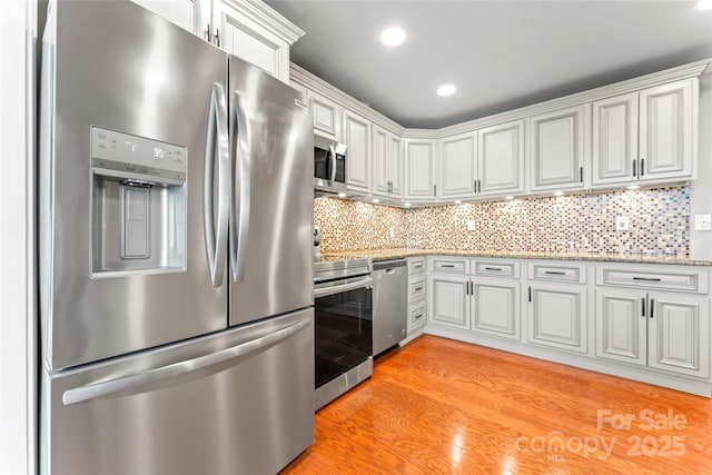 kitchen featuring light stone counters, stainless steel appliances, backsplash, white cabinetry, and light wood-type flooring