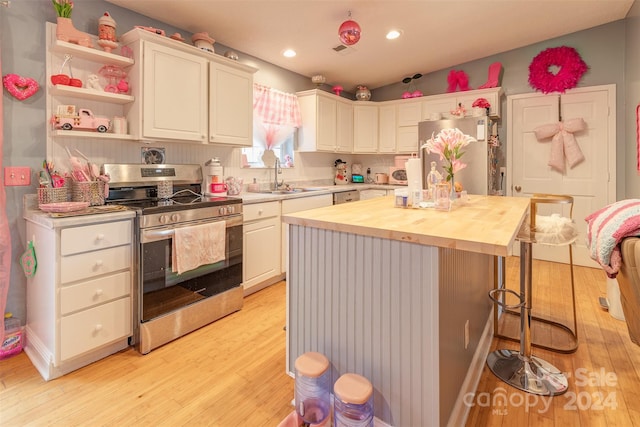 kitchen with stainless steel appliances, butcher block counters, light hardwood / wood-style floors, white cabinetry, and a breakfast bar area