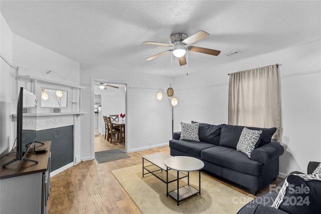 living room featuring light wood-type flooring, a textured ceiling, and ceiling fan