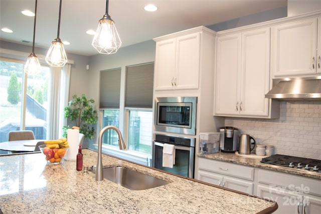 kitchen with sink, appliances with stainless steel finishes, decorative light fixtures, white cabinets, and exhaust hood