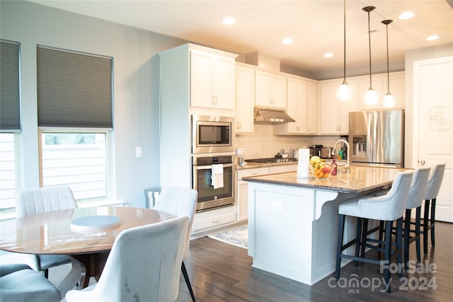 kitchen featuring white cabinets, an island with sink, dark hardwood / wood-style floors, appliances with stainless steel finishes, and decorative light fixtures