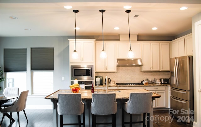 kitchen with ventilation hood, light stone counters, stainless steel appliances, hanging light fixtures, and sink