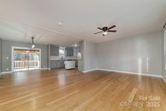 unfurnished living room featuring ceiling fan, light wood-type flooring, and sink