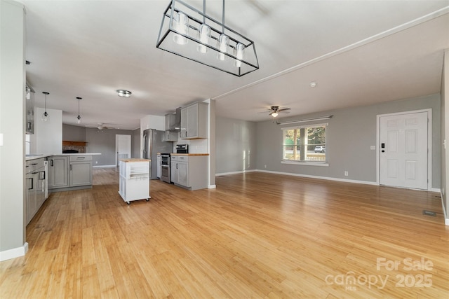 kitchen with gray cabinetry, stainless steel appliances, wall chimney range hood, pendant lighting, and a kitchen island