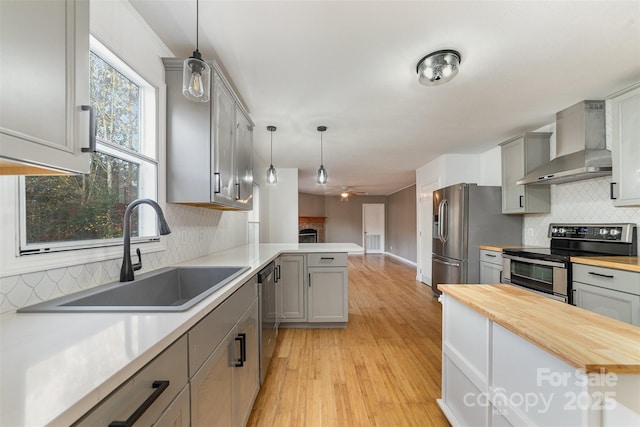 kitchen featuring wall chimney exhaust hood, gray cabinetry, stainless steel appliances, pendant lighting, and butcher block countertops