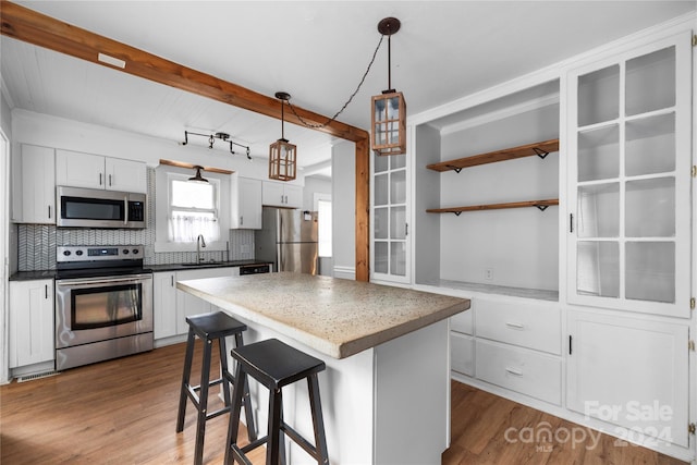 kitchen with a center island, white cabinets, decorative light fixtures, and stainless steel appliances