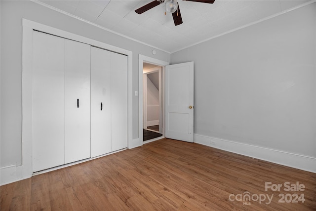 unfurnished bedroom with hardwood / wood-style floors, ceiling fan, crown molding, and a closet