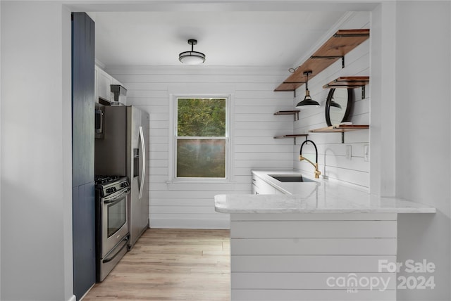 kitchen featuring stainless steel appliances, white cabinetry, sink, light stone countertops, and light wood-type flooring