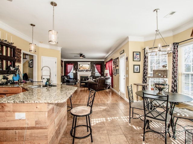 kitchen with light stone countertops, sink, hanging light fixtures, crown molding, and light wood-type flooring