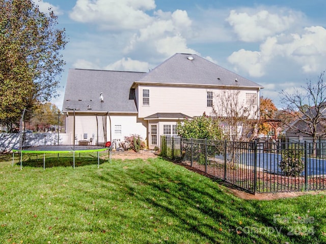 back of property with a trampoline and a lawn