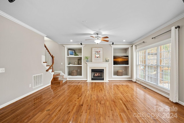 unfurnished living room featuring built in shelves, light hardwood / wood-style floors, ceiling fan, and crown molding