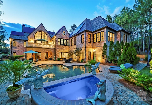 back house at dusk with a pool with hot tub, a patio area, and a balcony