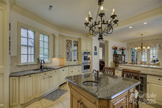 kitchen featuring sink, pendant lighting, double oven, and a center island with sink