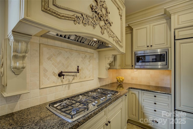 kitchen featuring appliances with stainless steel finishes, dark stone countertops, cream cabinetry, and backsplash