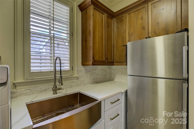 kitchen with stainless steel fridge, backsplash, light stone countertops, white cabinets, and sink