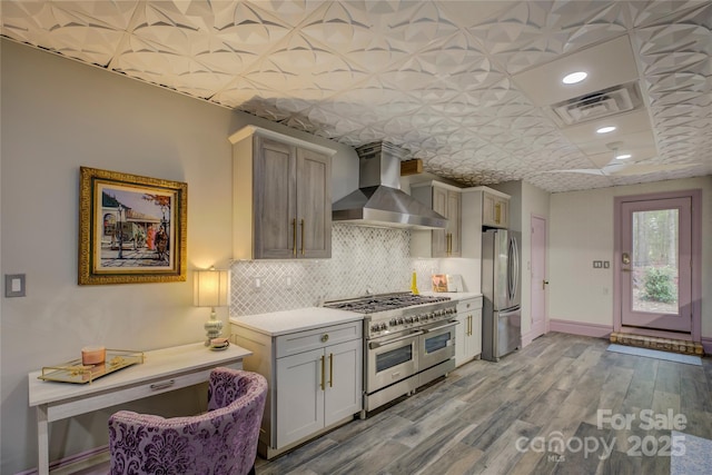 kitchen featuring backsplash, wall chimney range hood, light hardwood / wood-style floors, appliances with stainless steel finishes, and gray cabinetry