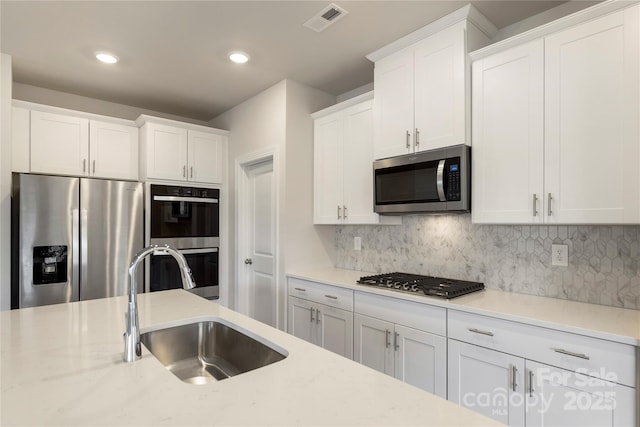 kitchen featuring light stone countertops, sink, stainless steel appliances, decorative backsplash, and white cabinets