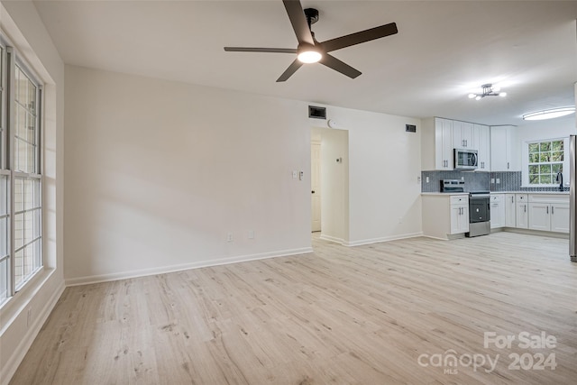 kitchen with backsplash, appliances with stainless steel finishes, white cabinets, ceiling fan, and light hardwood / wood-style flooring