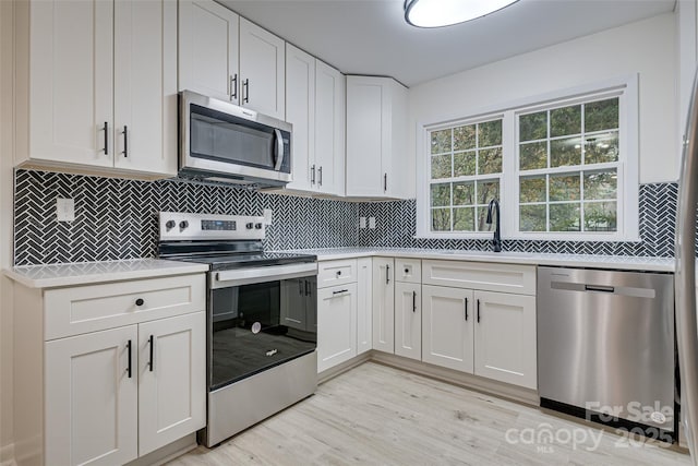 kitchen featuring sink, light hardwood / wood-style flooring, appliances with stainless steel finishes, white cabinets, and backsplash