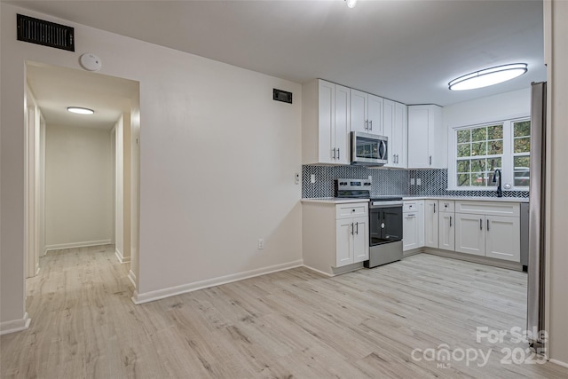 kitchen with appliances with stainless steel finishes, white cabinetry, sink, backsplash, and light hardwood / wood-style flooring