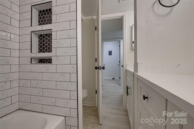 full bathroom featuring hardwood / wood-style flooring, tiled shower / bath, vanity, and toilet