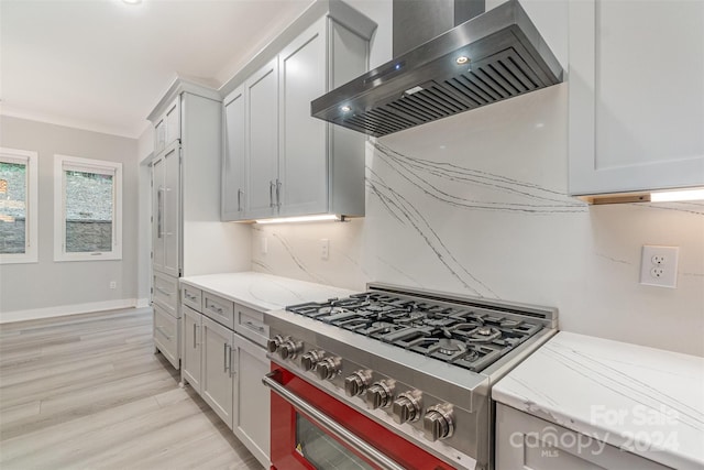 kitchen with light stone countertops, ornamental molding, wall chimney exhaust hood, light hardwood / wood-style floors, and stainless steel stove