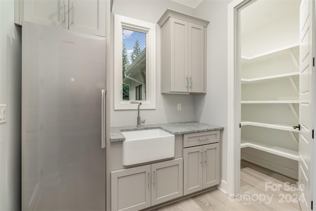 interior space with gray cabinets, light hardwood / wood-style floors, light stone countertops, and sink