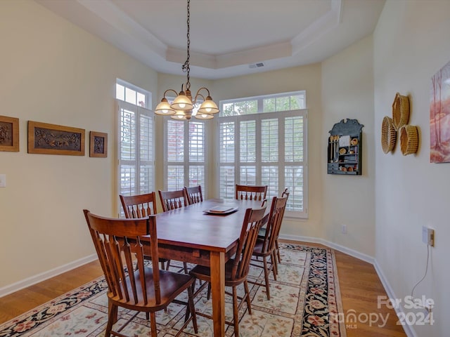 dining space with a tray ceiling, an inviting chandelier, and light hardwood / wood-style flooring