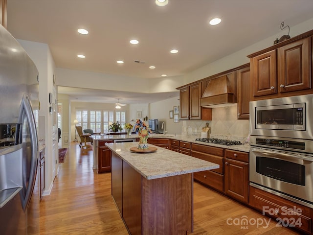 kitchen with kitchen peninsula, light hardwood / wood-style floors, custom exhaust hood, and appliances with stainless steel finishes