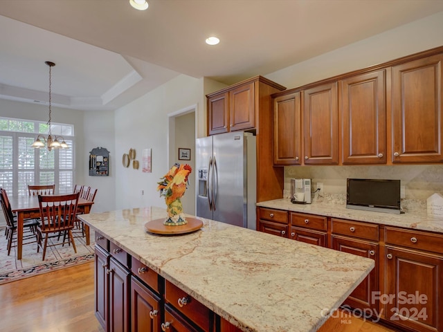 kitchen featuring light hardwood / wood-style floors, light stone counters, stainless steel refrigerator with ice dispenser, hanging light fixtures, and a kitchen island