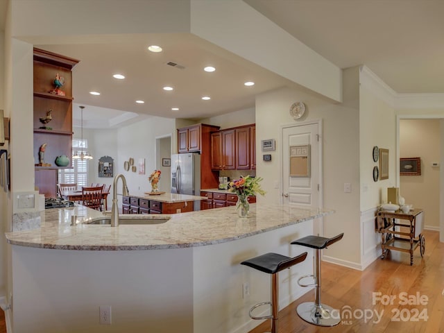 kitchen with sink, light stone counters, kitchen peninsula, stainless steel refrigerator with ice dispenser, and light hardwood / wood-style flooring