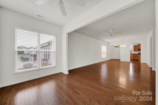 empty room featuring dark hardwood / wood-style floors, a healthy amount of sunlight, and ceiling fan with notable chandelier