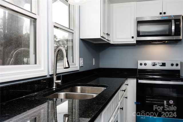 kitchen featuring stainless steel appliances, dark stone countertops, white cabinetry, and sink