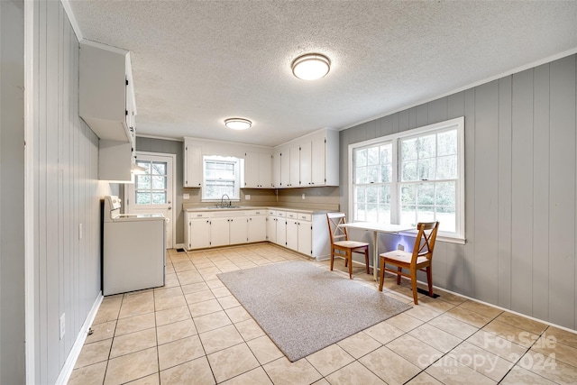 kitchen with light tile patterned flooring, stove, wooden walls, sink, and white cabinets