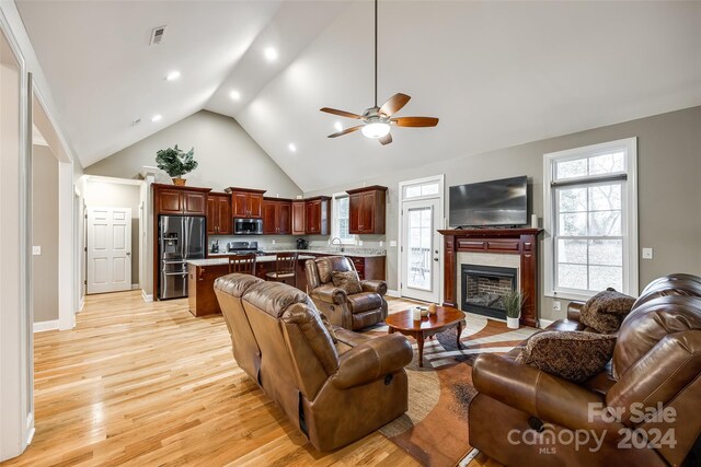 living room featuring light hardwood / wood-style floors, a tiled fireplace, sink, ceiling fan, and high vaulted ceiling