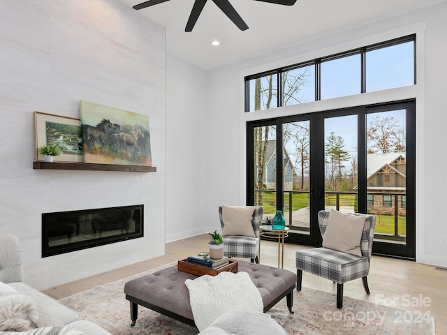 living room with ceiling fan, a large fireplace, light hardwood / wood-style floors, and a high ceiling