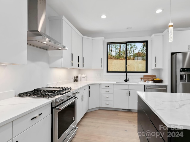 kitchen with appliances with stainless steel finishes, white cabinetry, hanging light fixtures, and wall chimney exhaust hood