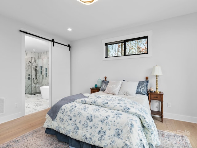 bedroom with hardwood / wood-style floors, a barn door, and ensuite bath